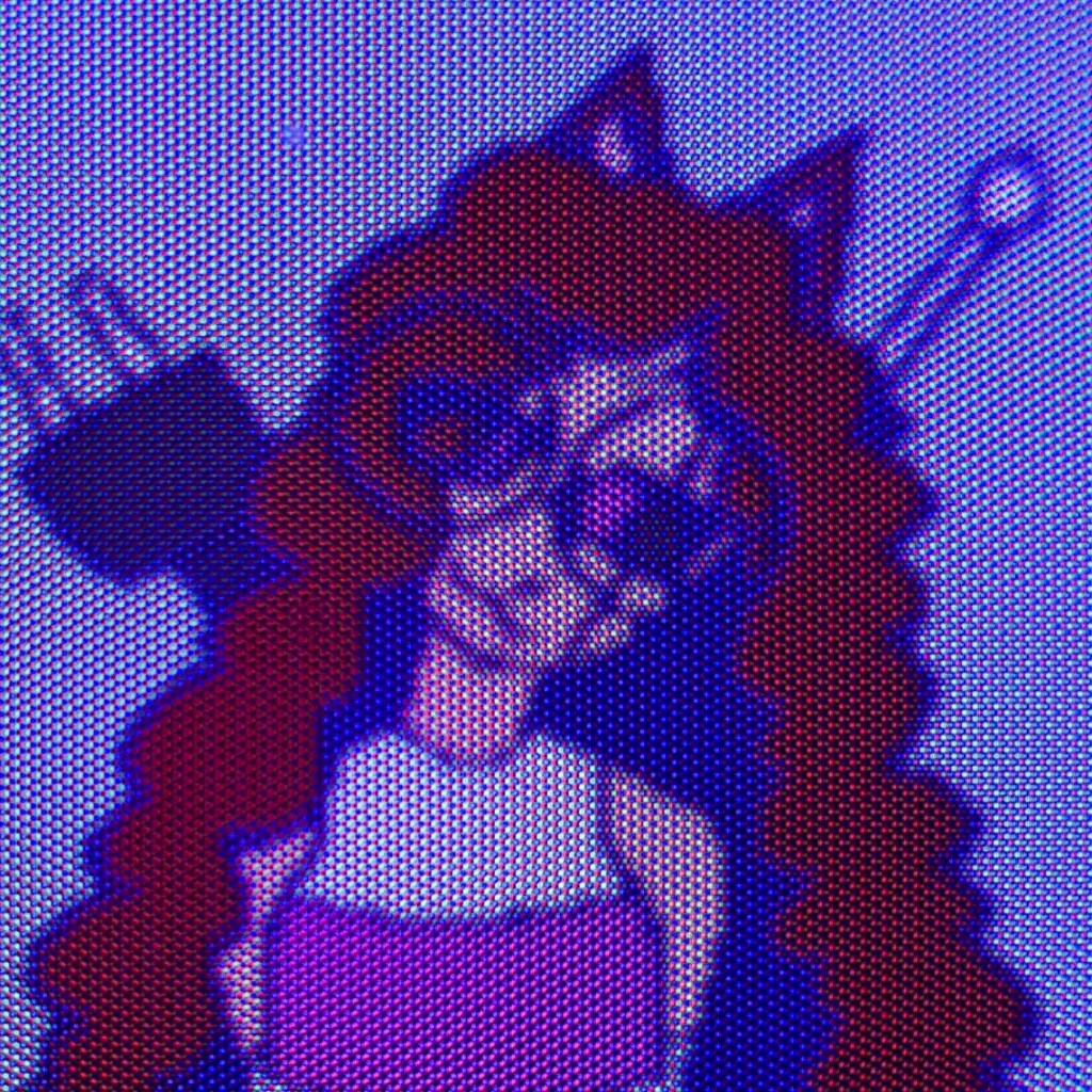 An up-close picture of a CRT displaying a brown haired catgirl tilting it's head and giving a smug smile